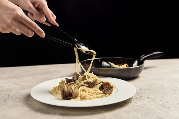 Partial view of woman putting delicious Italian spaghetti with seafood on plate isolated on black — Stock Photo