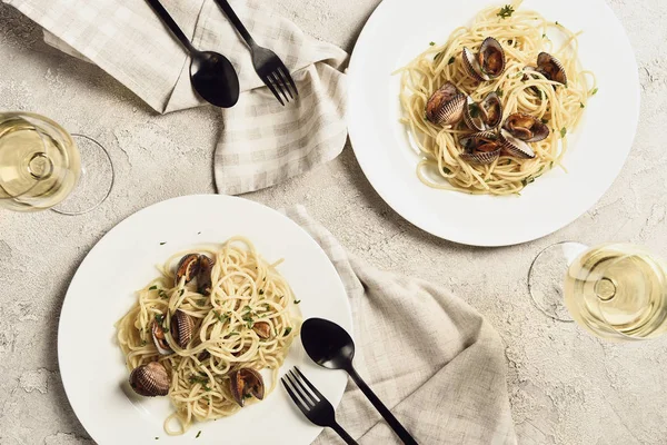 Blick von oben auf köstliche Pasta mit Meeresfrüchten serviert mit Weißwein für zwei Personen auf strukturierter grauer Oberfläche — Stockfoto