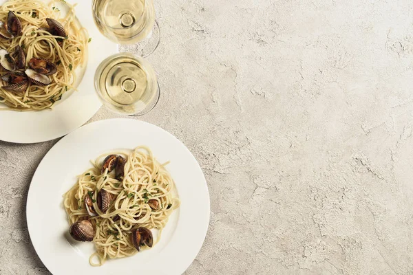 Draufsicht auf köstliche Pasta mit Meeresfrüchten serviert mit Weißwein in Gläsern auf strukturierter grauer Oberfläche mit Kopierfläche — Stockfoto