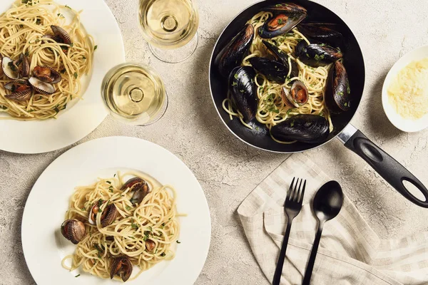 Draufsicht auf köstliche Pasta mit Meeresfrüchten serviert mit Weißwein auf texturierter grauer Oberfläche — Stockfoto