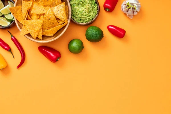 Draufsicht auf knusprige Nachos, Guacamole und Gewürze auf orangefarbenem Hintergrund mit Kopierraum — Stockfoto