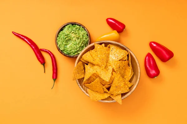 Vista superior de nachos mexicanos crujientes, guacamole, chile y pimientos sobre fondo naranja - foto de stock