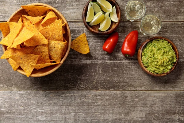 Top view of nachos served with guacamole, peppers, limes and Tequila on weathered wooden table — Stock Photo