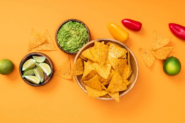 Top view of crispy Mexican nachos, guacamole,peppers and limes on orange background — Stock Photo