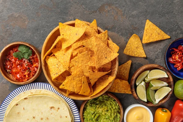 Top view of Mexican nachos served with tortilla, guacamole, cheese sauce and salsa on stone table — Stock Photo