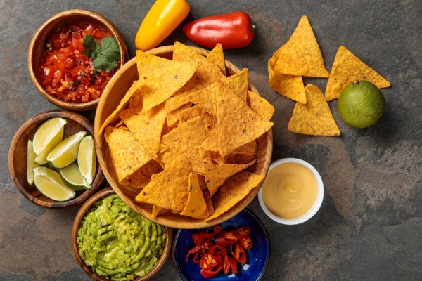 Top view of Mexican nachos served with guacamole, limes, cheese sauce and salsa on stone table — Stock Photo