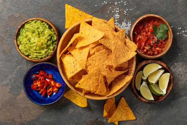 Vista superior de nachos mexicanos servidos com guacamole, limas, pimentas e salsa na mesa de pedra — Fotografia de Stock