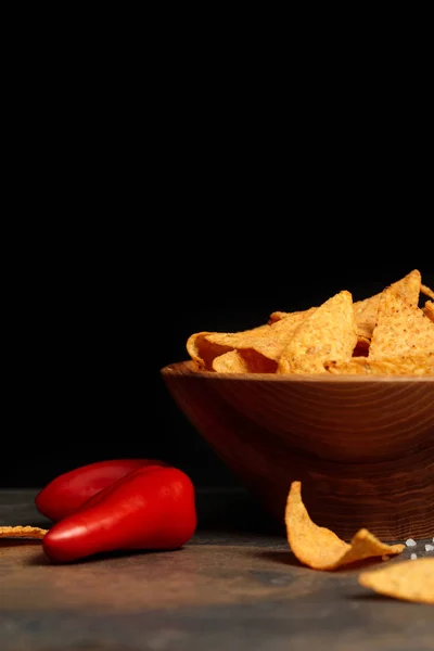 Delicious crunchy Mexican nachos with salt and chili peppers on stone table isolated on black — Stock Photo