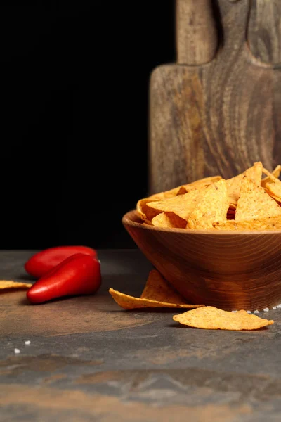 Mexican nachos with salt and chili peppers near wooden cutting boards on stone table isolated on black — Stock Photo