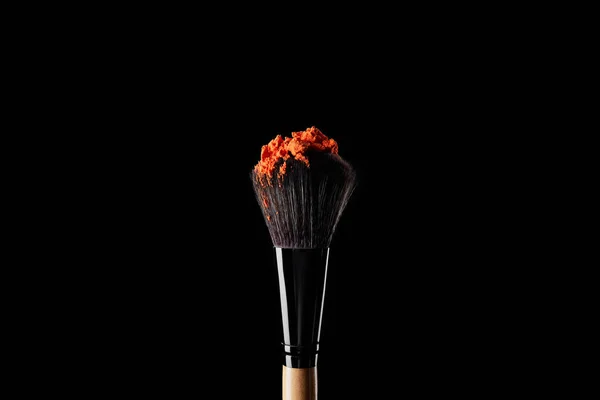 Cosmetic brush with colorful orange powder isolated on black — Stock Photo