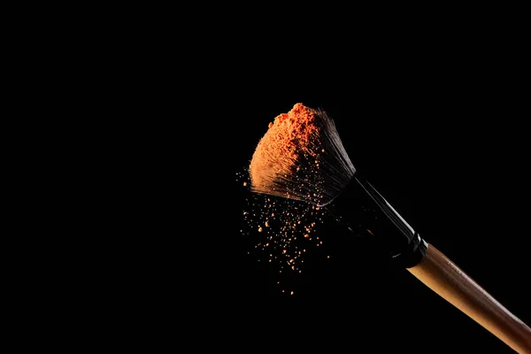 Cepillo cosmético con polvo de naranja sobre fondo negro - foto de stock