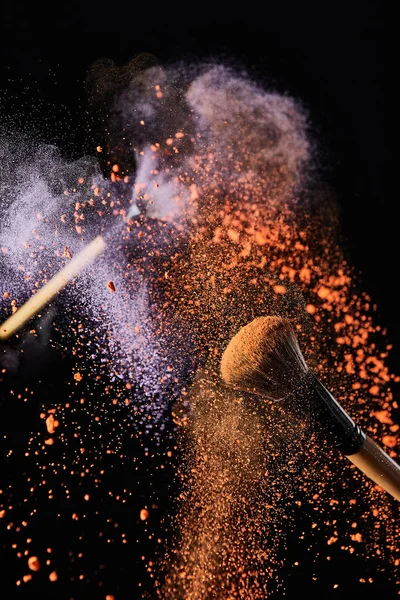 Pennelli cosmetici con colorato arancione e viola esplosione polvere su sfondo nero — Foto stock