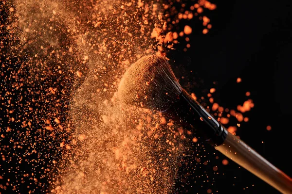 Cosmetic brush with colorful orange powder explosion — Stock Photo