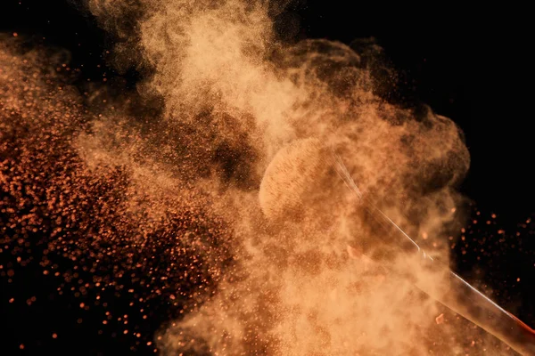 Cepillo cosmético con colorida explosión de polvo naranja sobre fondo negro - foto de stock