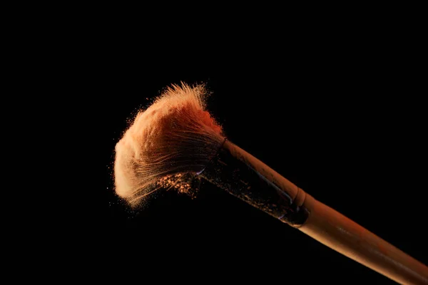 Cosmetic brush with colorful orange powder on black background — Stock Photo