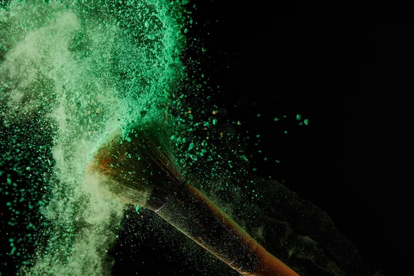 Soft cosmetic brush with colorful green powder explosion on black background — Stock Photo