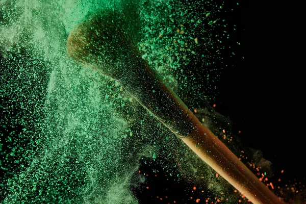 Brosse cosmétique avec explosion de poudre verte sur fond noir — Photo de stock