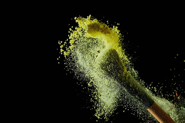 Cosmetic brush with colorful yellow powder explosion on black background — Stock Photo