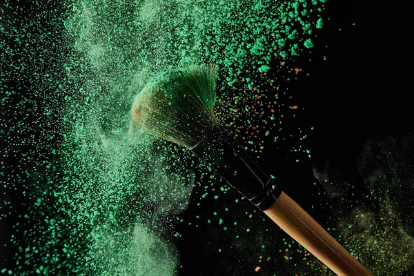 Cosmetic brush with green powder explosion on black background — Stock Photo