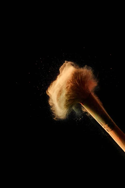 Cosmetic brush with colorful orange powder explosion on black background with copy space — Stock Photo