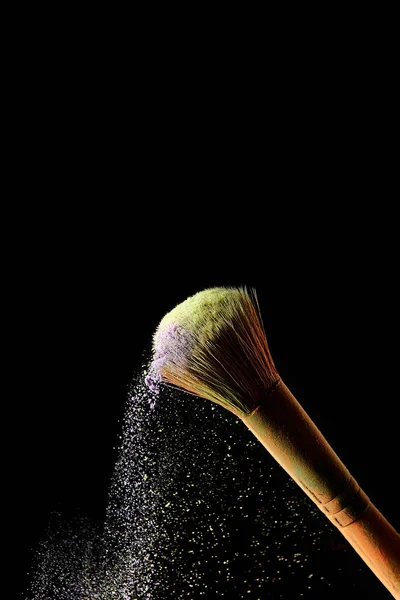 Cepillo cosmético con colorido polvo dispersado amarillo y violeta sobre fondo negro - foto de stock