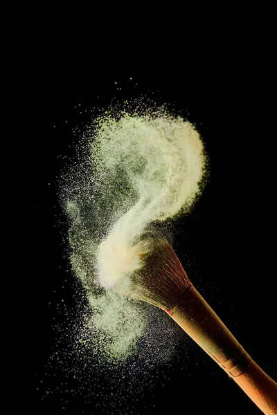 Cepillo cosmético con polvo disperso de color amarillo sobre fondo negro - foto de stock