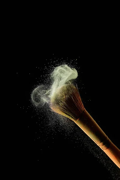 Cosmetic brush with yellow colorful powder on black background — Stock Photo