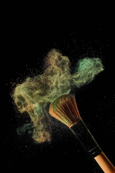 Cosmetic brush with green and orange powder explosion on black background — Stock Photo