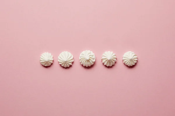 Pose plate avec des meringues blanches douces en rangée horizontale sur fond rose — Photo de stock