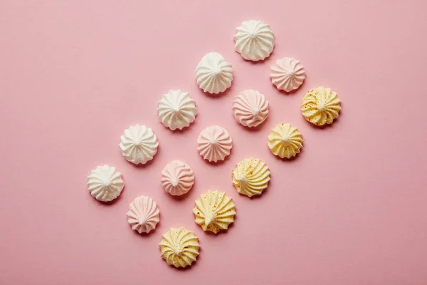 Vue de dessus des meringues blanches, roses et jaunes en rangées sur fond rose — Photo de stock