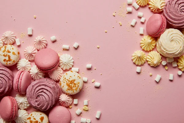 Top view of delicious sweet macaroons, meringues and marshmallows with yellow pieces on pink background — Stock Photo