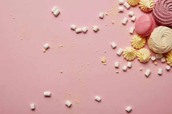 Vue de dessus de macarons roses doux, meringues et guimauves avec des morceaux jaunes sur fond rose — Photo de stock