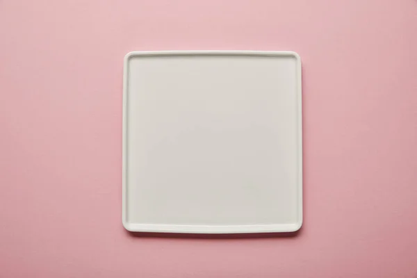 Vista superior de la placa plana cuadrada blanca sobre fondo rosa - foto de stock