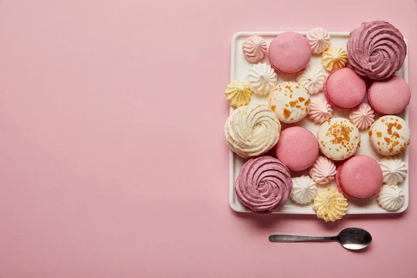 Flat lay with assorted meringues and macaroons on square dish with spoon on pink background — Stock Photo