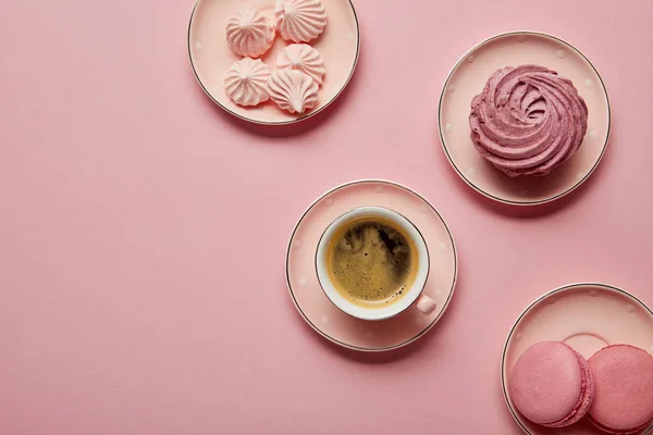 Draufsicht auf rosa gepunktete Untertassen mit Baiser, Makronen und Tasse Kaffee auf rosa Hintergrund — Stockfoto