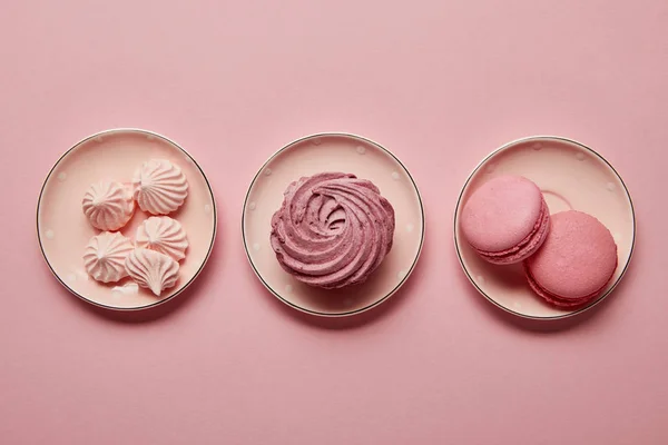 Flat lay with pink meringues and macaroons on pink dotted saucers on pink background — Stock Photo