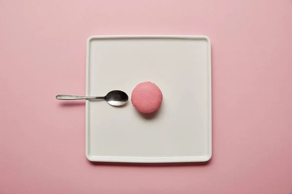 Top view on pink macaroon with teaspoon on white square dish on pink background — Stock Photo