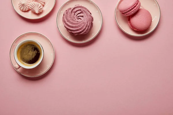 Top view of pink meringues, macaroons and cup of coffee on pink saucers with white dots on pink background — Stock Photo