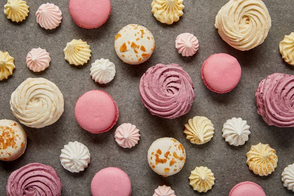 Vue de dessus des macarons assortis rose blanc et jaune avec des meringues sur fond gris — Photo de stock