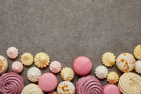 Top view of pink and white macaroons with pink, yellow and white meringues on gray background — Stock Photo