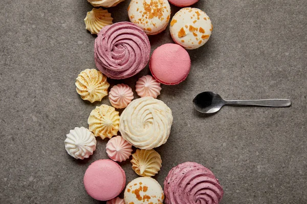 Vista superior de macarrones rosados y blancos con merengues rosados, amarillos y blancos con cucharadita sobre fondo gris — Stock Photo