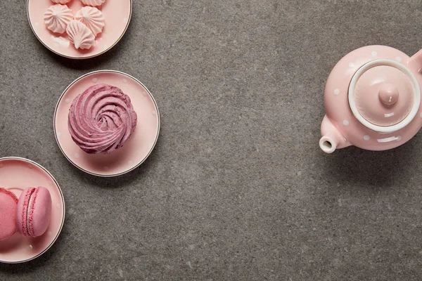 Top view of pink with dotted teapot and saucers with meringues and zephyr on gray background — Stock Photo