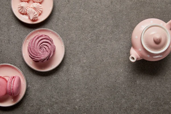 Вид сверху на розовый чайник и блюдца с мерингусами и розовыми гирями на светлом фоне — стоковое фото