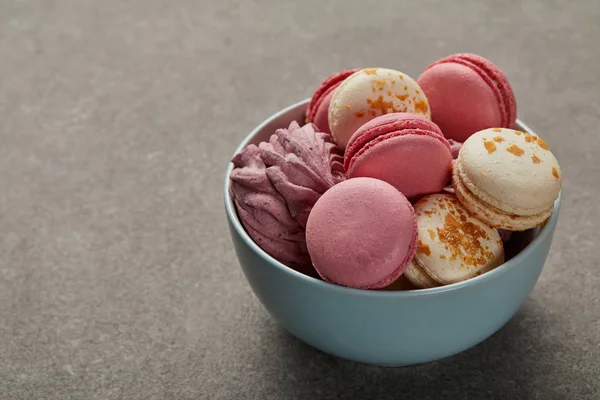 Blue bowl with assorted macaroons and pink zephyr on gray background — Stock Photo