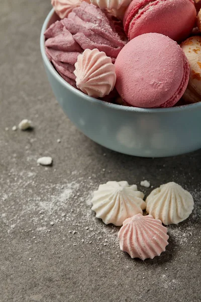 Cuenco azul con deliciosos macarrones franceses, suave zephyr y pequeños merengues rosados y blancos con trozos de azúcar sobre fondo gris - foto de stock