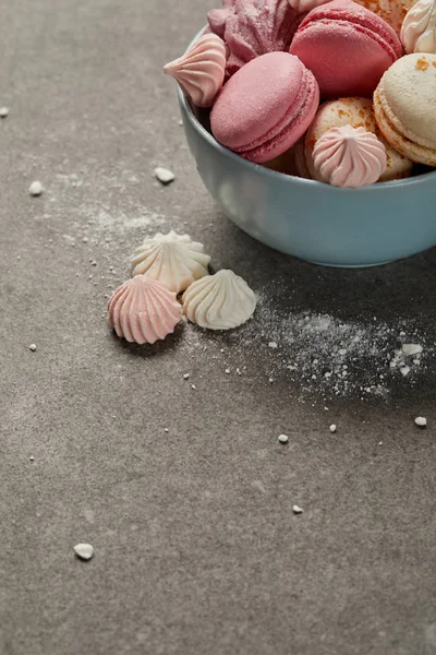 Tazón azul con macarrones rosados, zephyr suave y pequeños merengues rosados y blancos con trozos de azúcar sobre fondo gris — Stock Photo