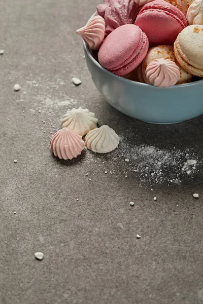 Bol bleu avec macarons roses, zéphyr doux et petites meringues roses et blanches avec morceaux de sucre sur fond gris — Photo de stock