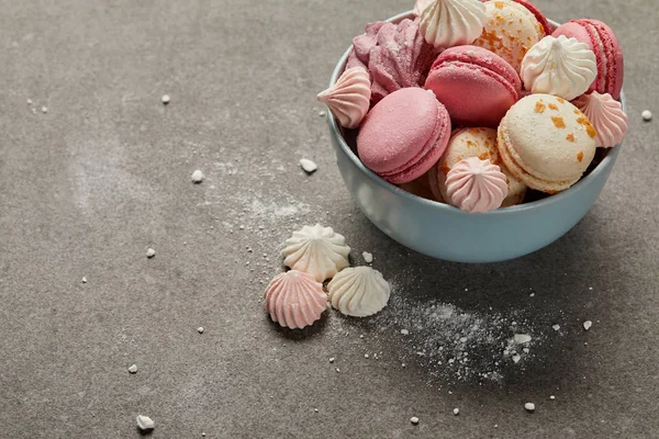 Deliciosos macarrones y merengues franceses en tazón azul y trozos de azúcar desmenuzados sobre fondo gris - foto de stock