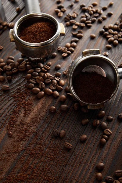 Portafilters filled with aromatic ground coffee on dark wooden surface with coffee beans — Stock Photo