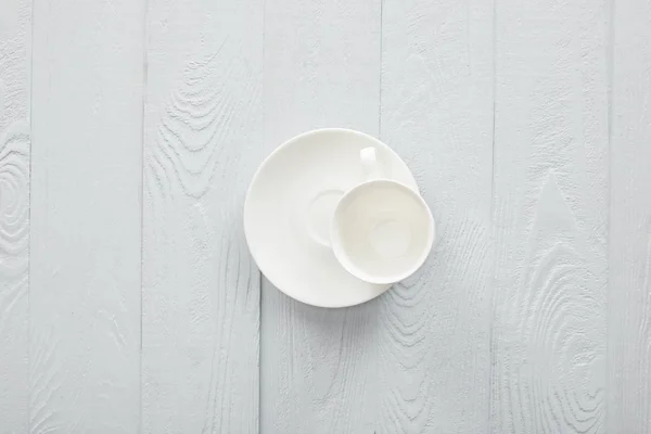 Vaciar taza blanca con platillo en la superficie de madera blanca - foto de stock